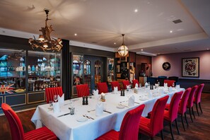 A formal dining room with a long table set for a meal, red upholstered chairs, and a chandelier. - Der LIPPISCHE HOF (Bad Salzuflen)