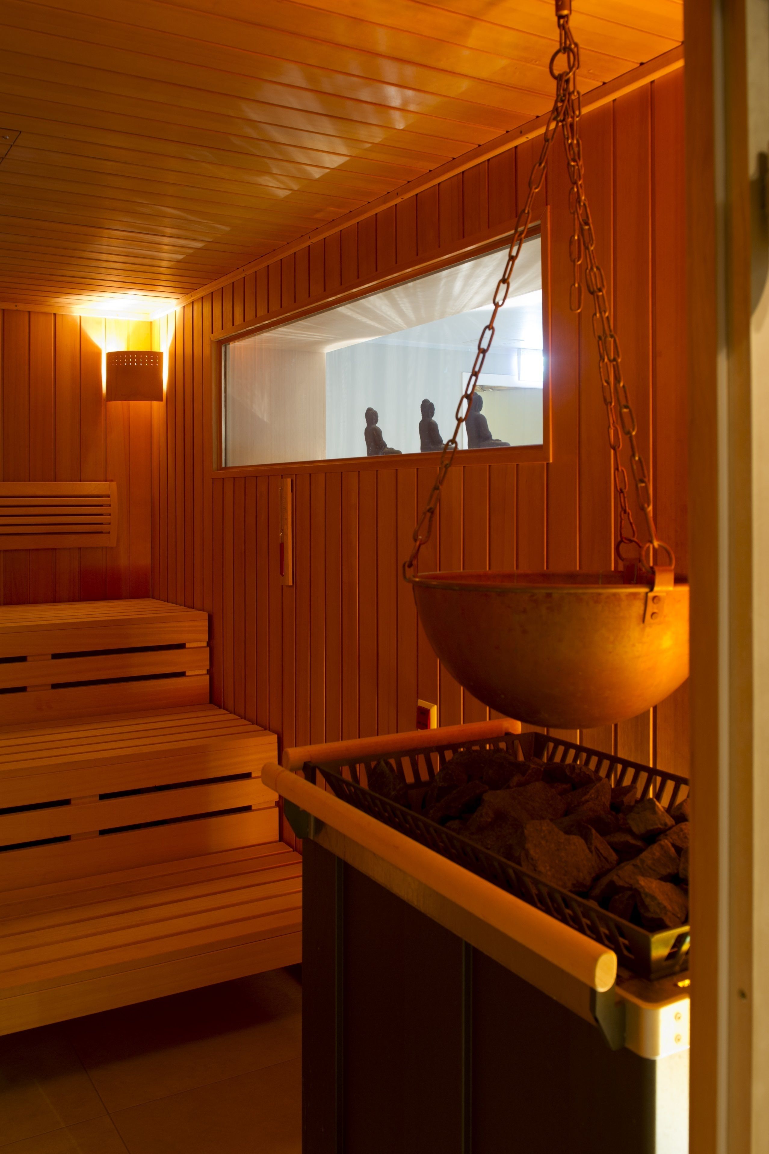 Un sauna avec des bancs en bois, un seau suspendu et une fenêtre donnant sur l’extérieur.