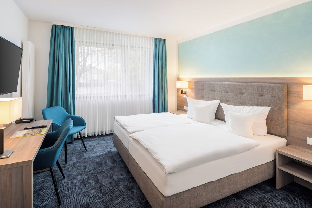 A hotel room with a large bed, a desk with a chair, a TV, and a window with curtains.