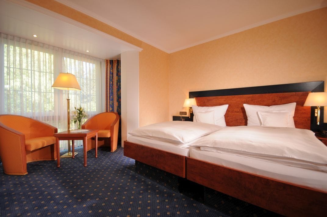 A hotel room with a large bed, two bedside tables, a chair, and a lamp.