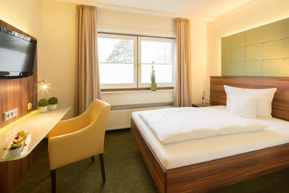 A hotel room with a bed, a desk, a chair, a TV, and a window with curtains.