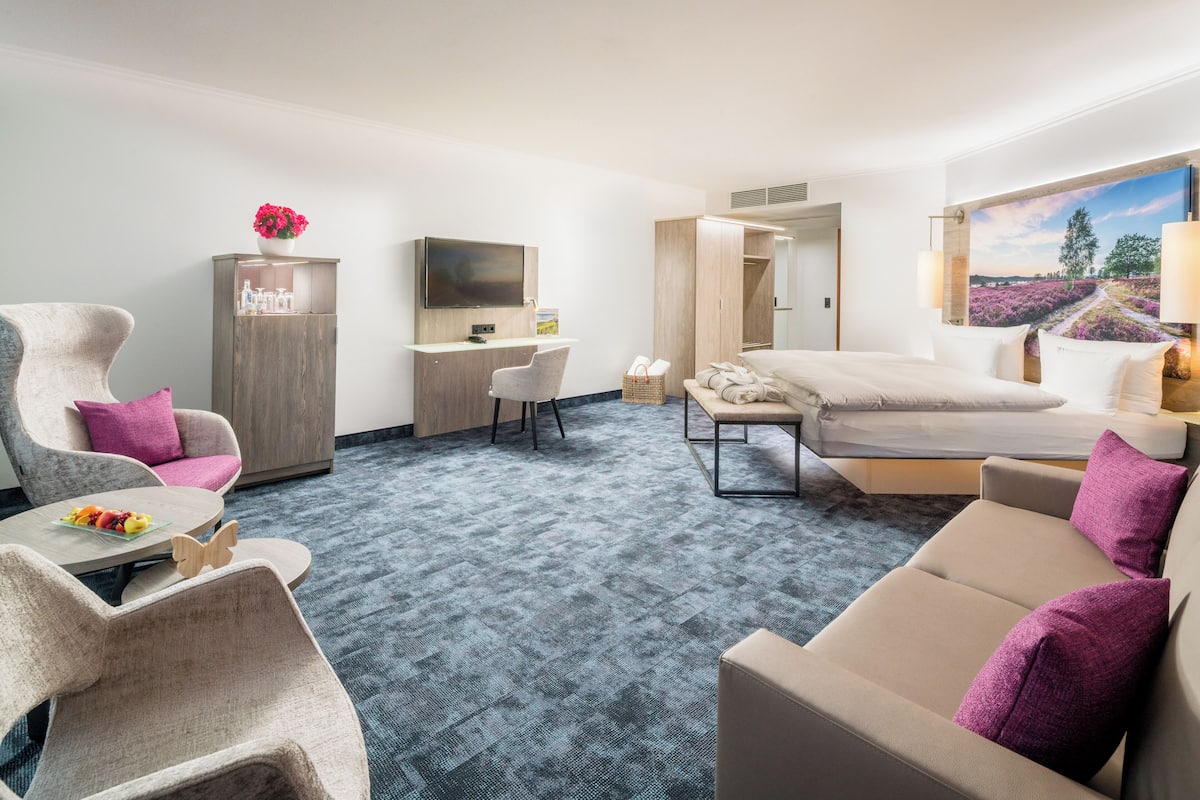 A hotel room with a sofa, armchair, desk, TV, and a bed.