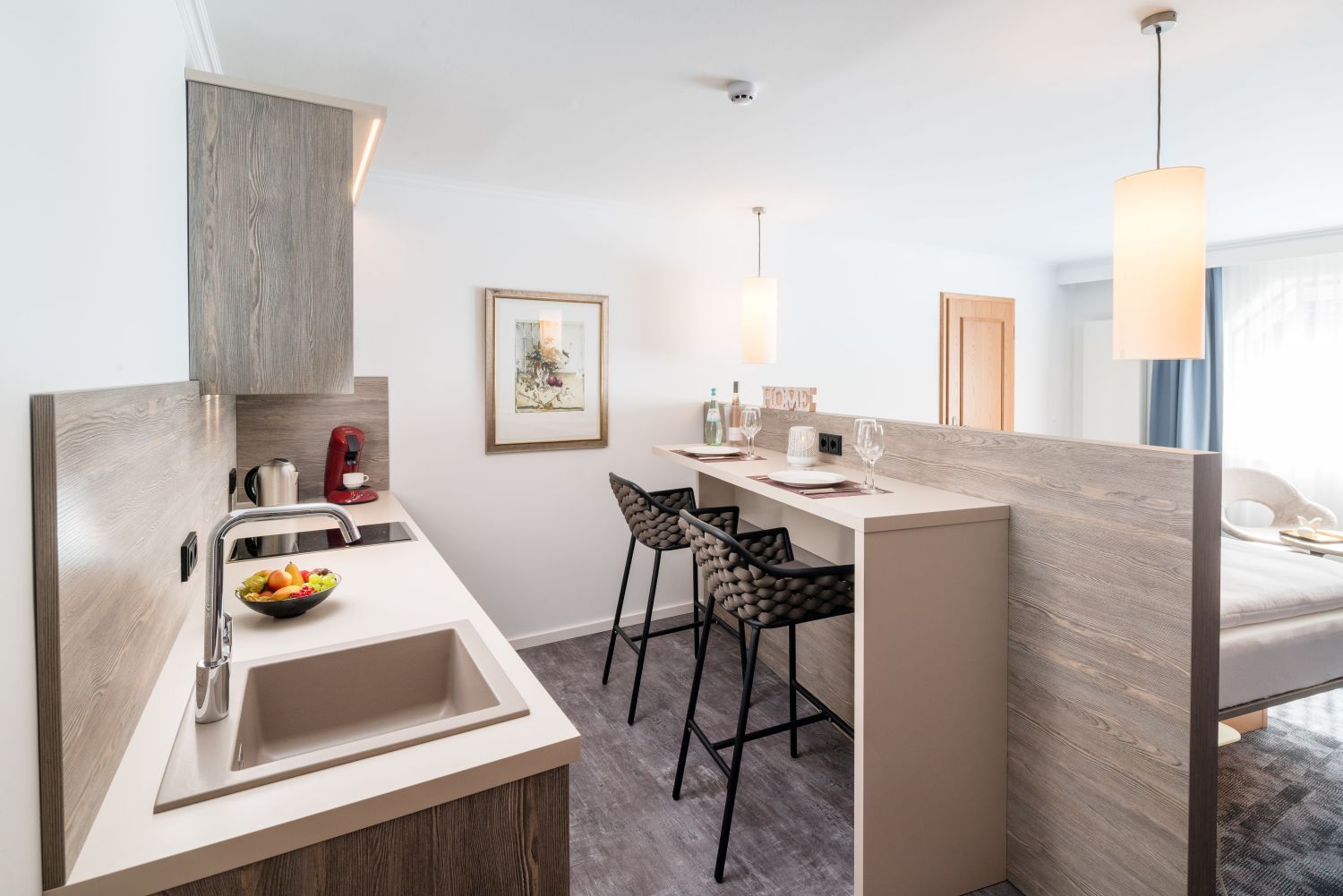 A modern hotel room with a kitchenette, a dining area, and a bed.