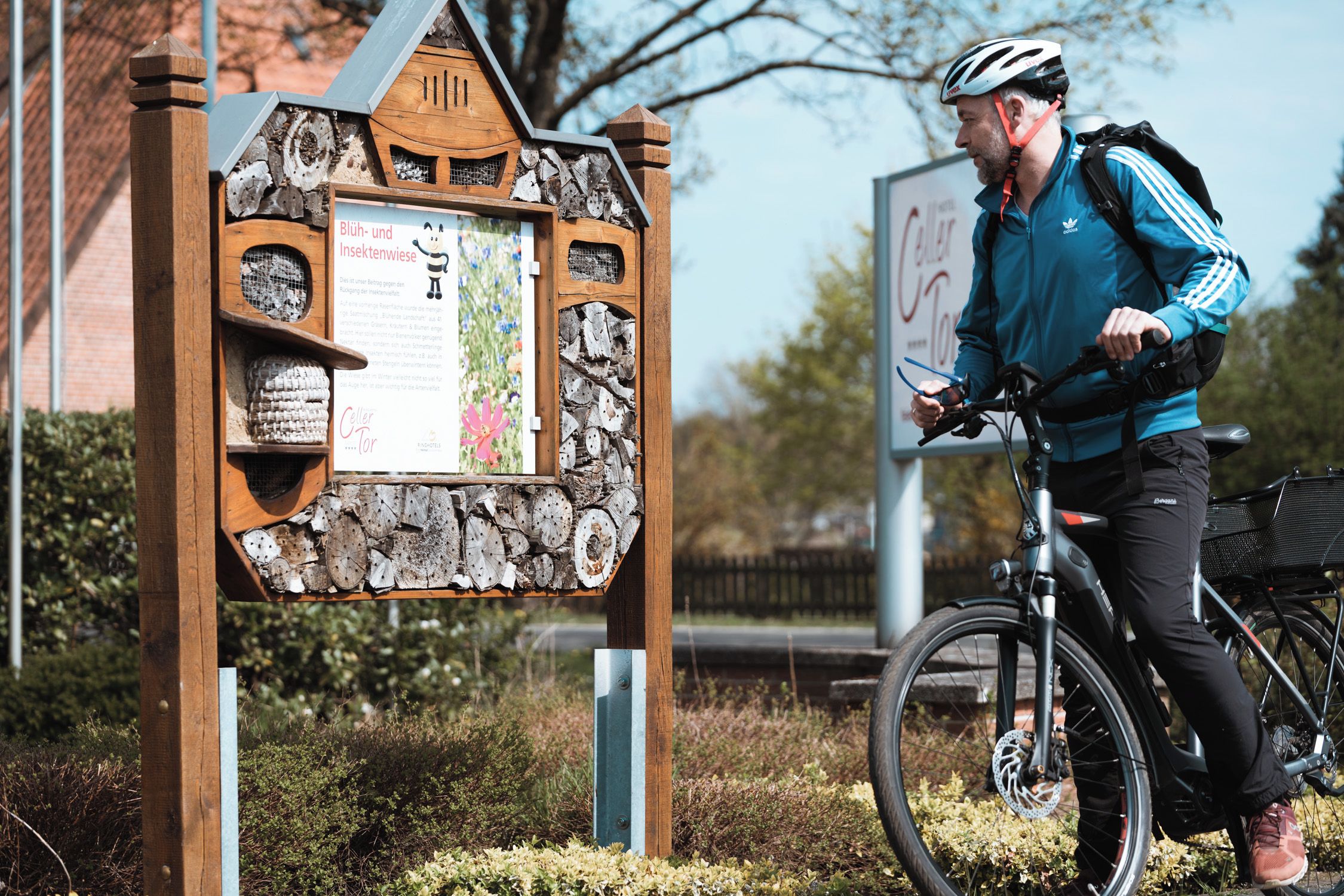 A wooden sign with text and a cyclist with a bicycle.