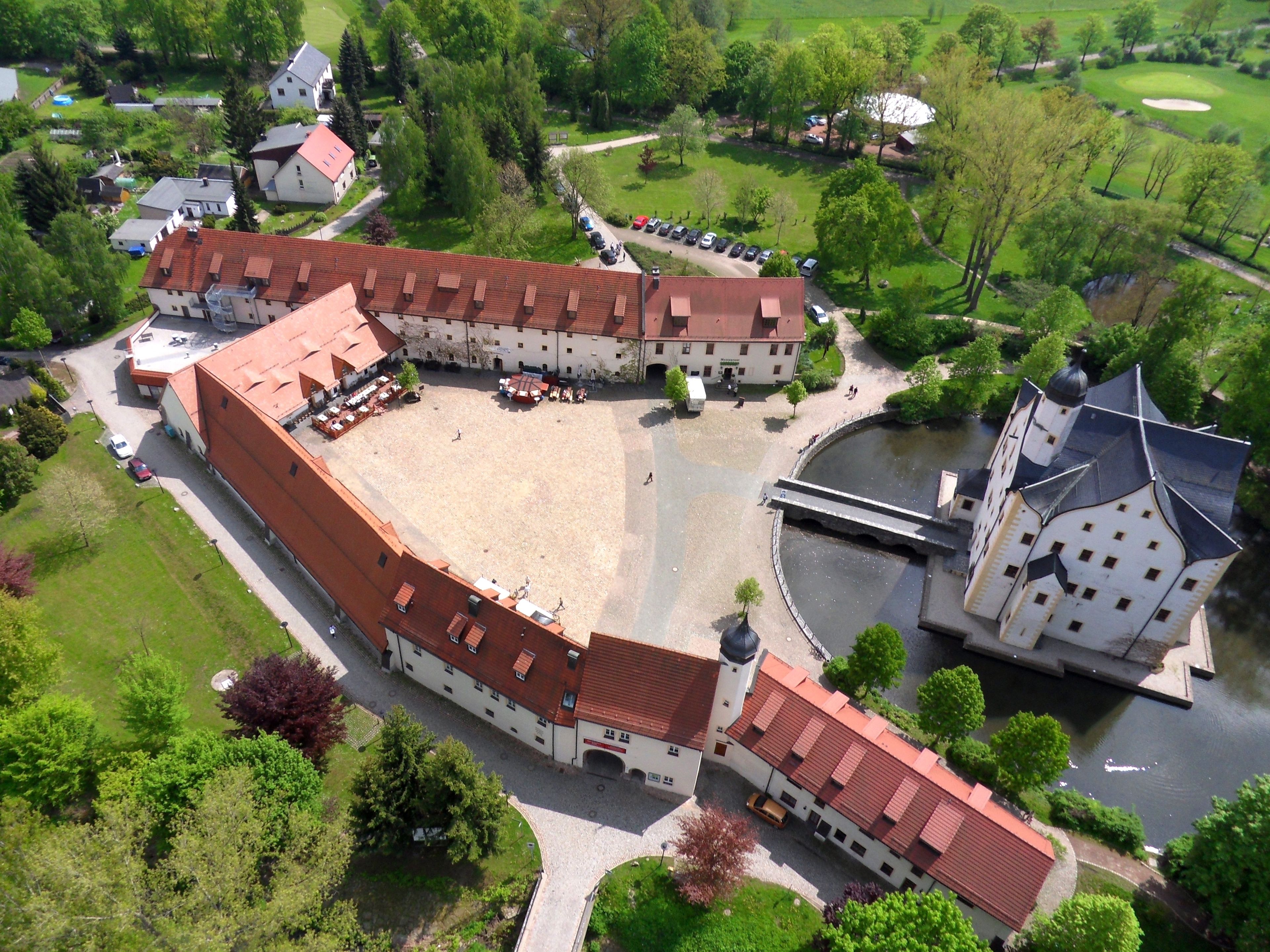 Vista aérea de un complejo de edificios históricos con un patio, un río y un campo de golf al fondo.