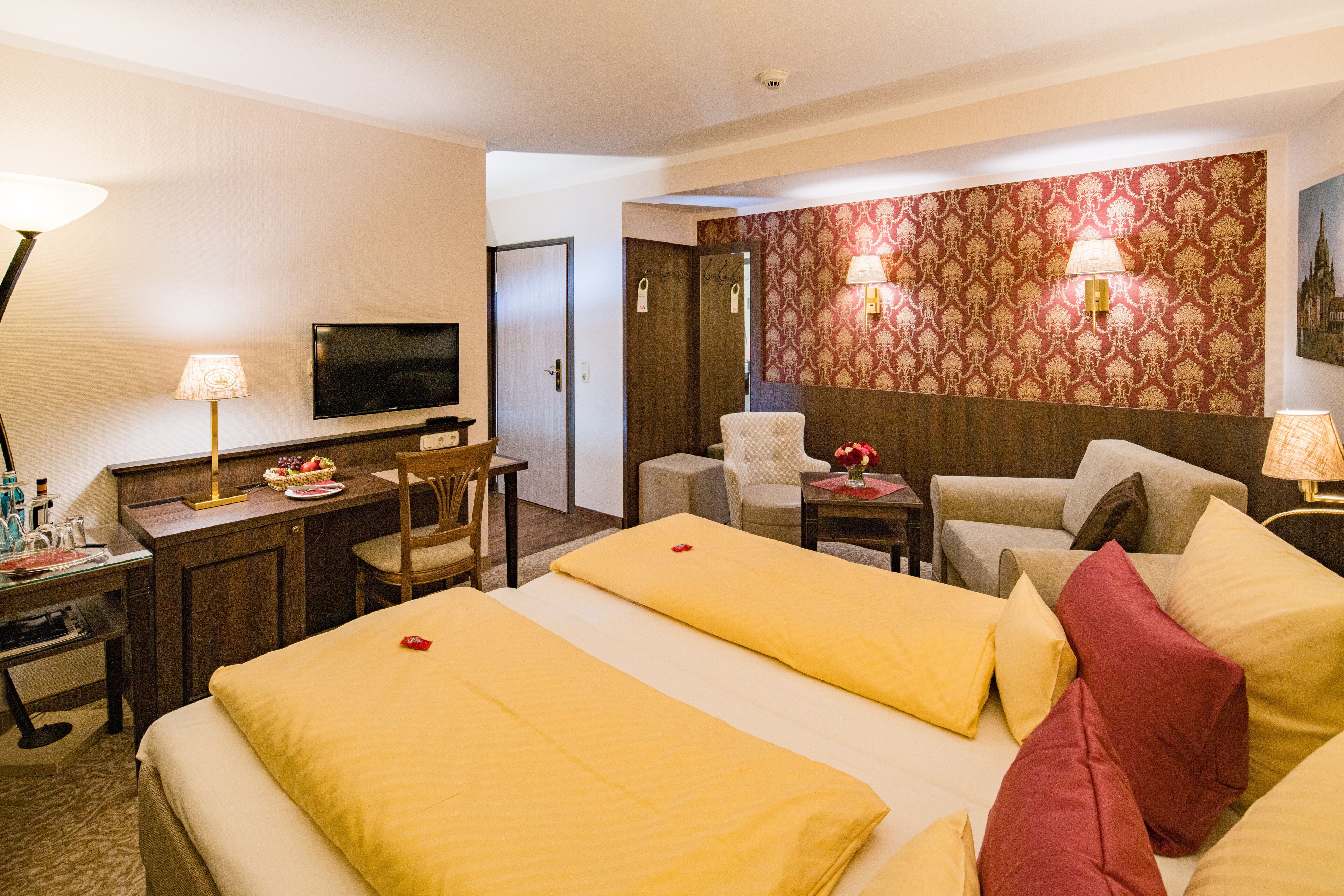 A hotel room with two beds, a desk with a television, a chair, a sofa, and a decorative wall.