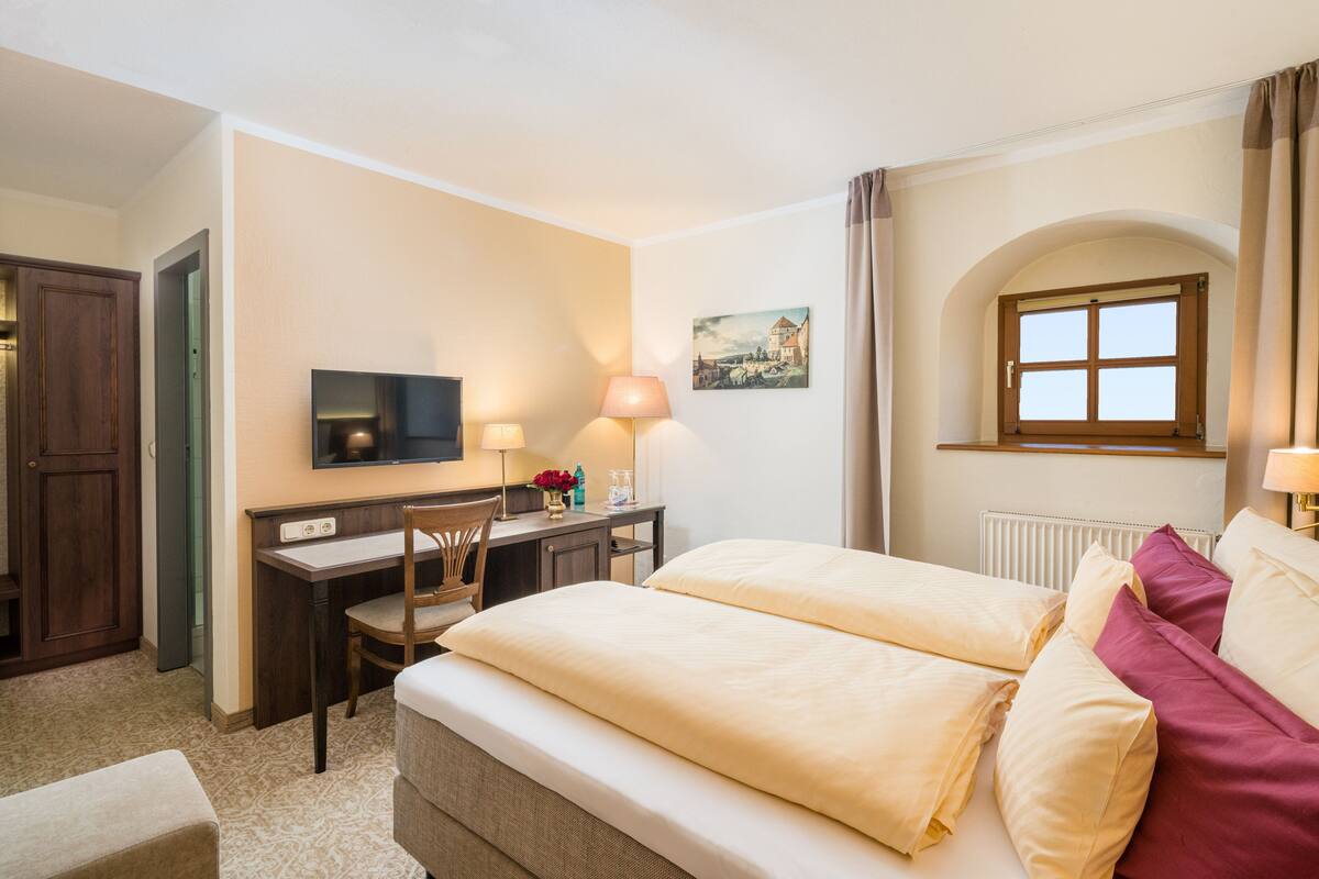 Une chambre d’hôtel équipée d’un lit, d’un bureau, d’une chaise, d’une télévision, d’une lampe et d’une fenêtre avec des rideaux.