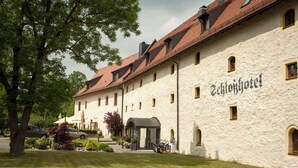A traditional building with a sign reading "Schloßhotel". It features a stone facade, multiple windows, and a red-tiled roof.