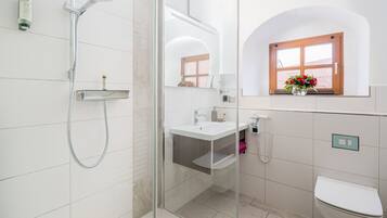 Ein modernes Badezimmer mit einer gläsernen Duschkabine, einem weißen Waschbecken, einer Toilette und einem Fenster mit Blumen.