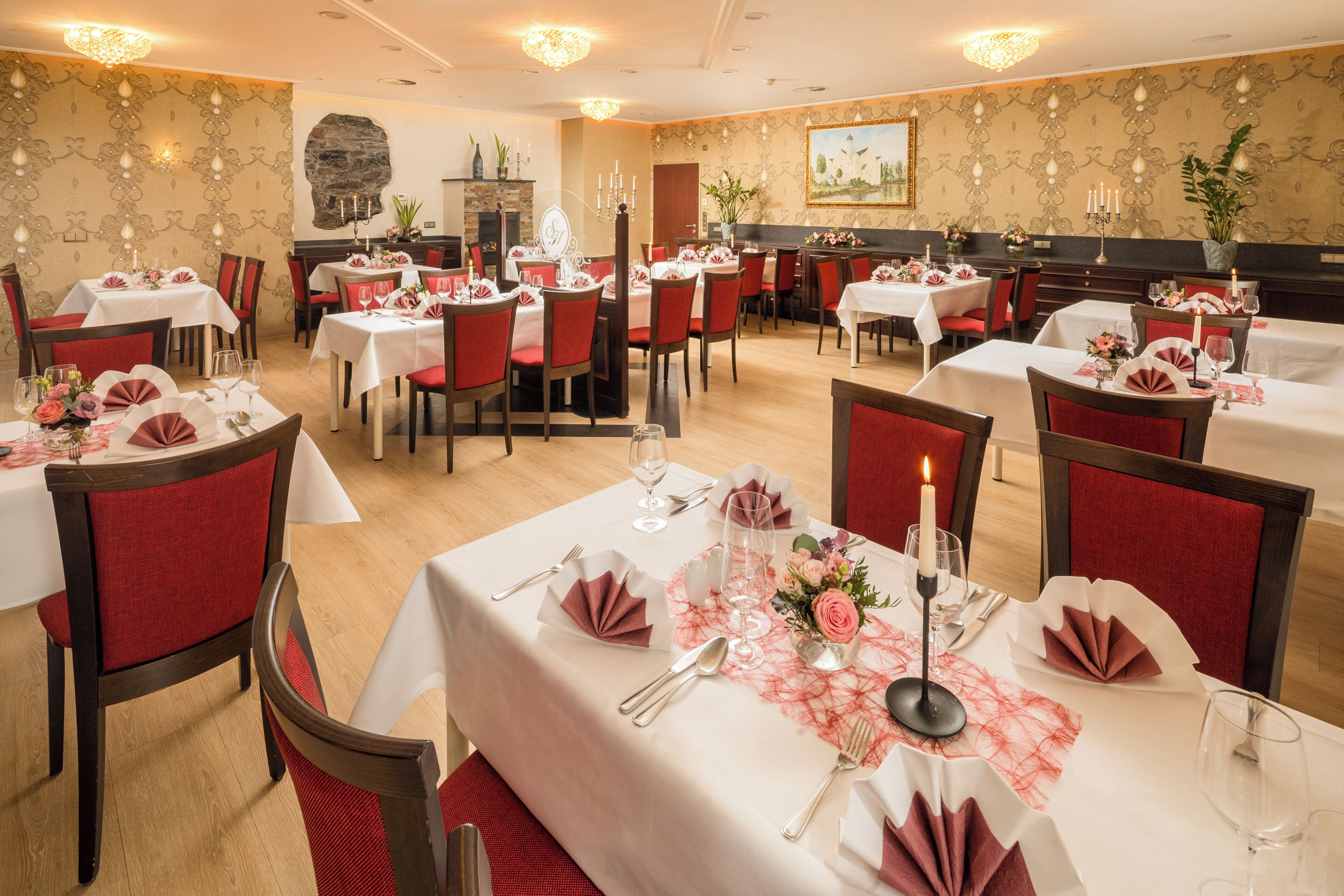 A restaurant with multiple tables set for dining, each with white tablecloths, red chairs, and floral centerpieces.