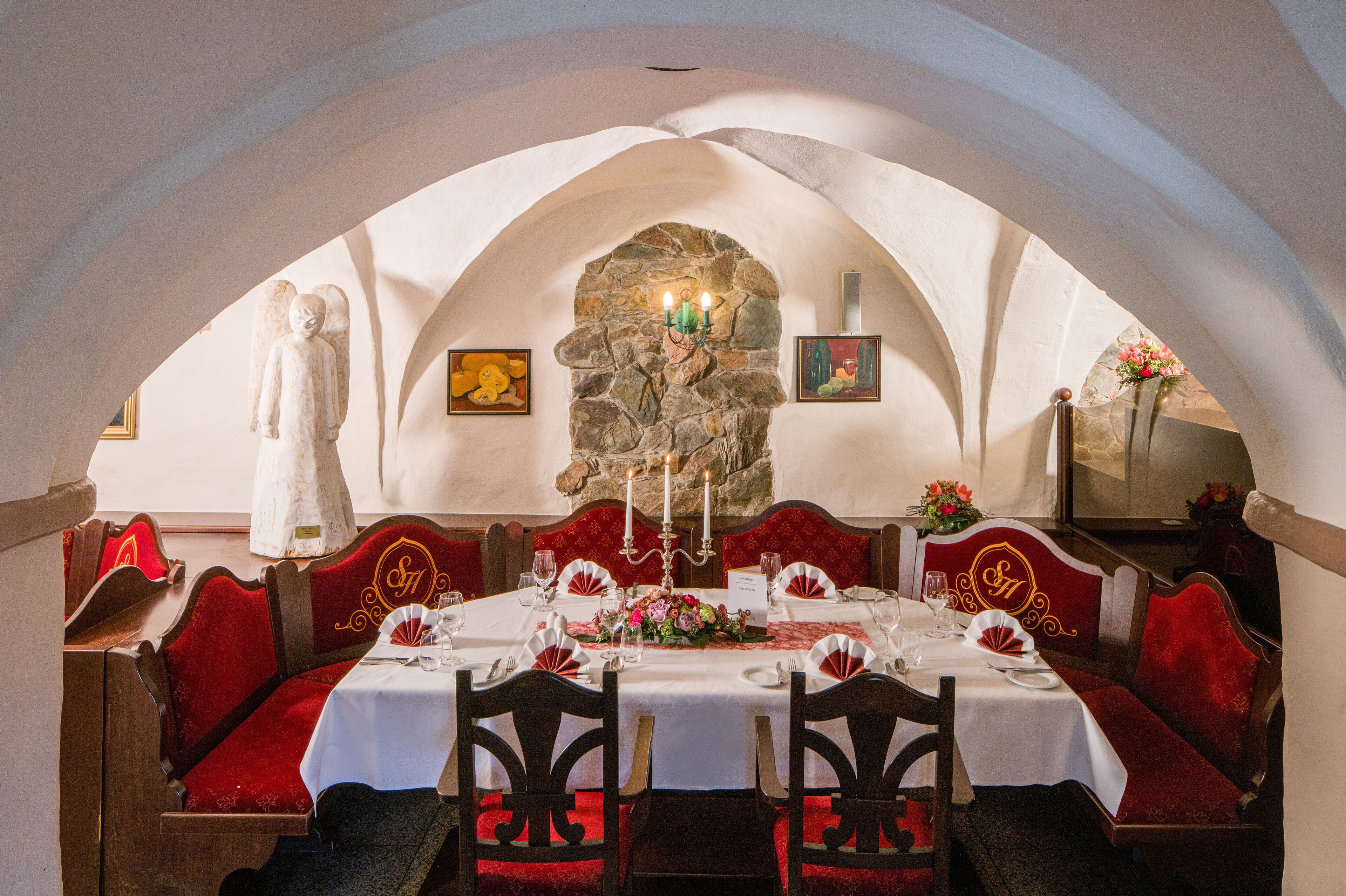 Comedor con chimenea de piedra, asientos tapizados en rojo y una mesa blanca para cuatro.