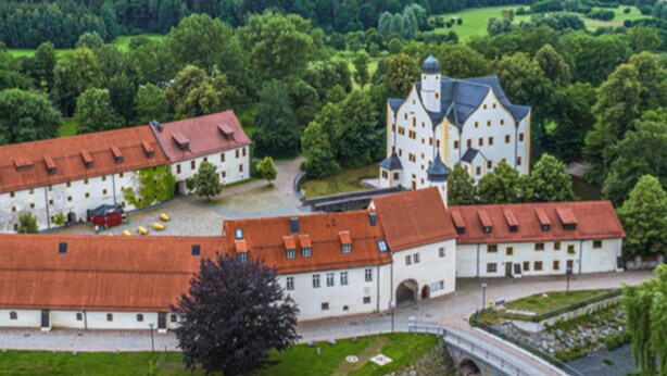 A large, historic building with a central courtyard, surrounded by lush greenery.