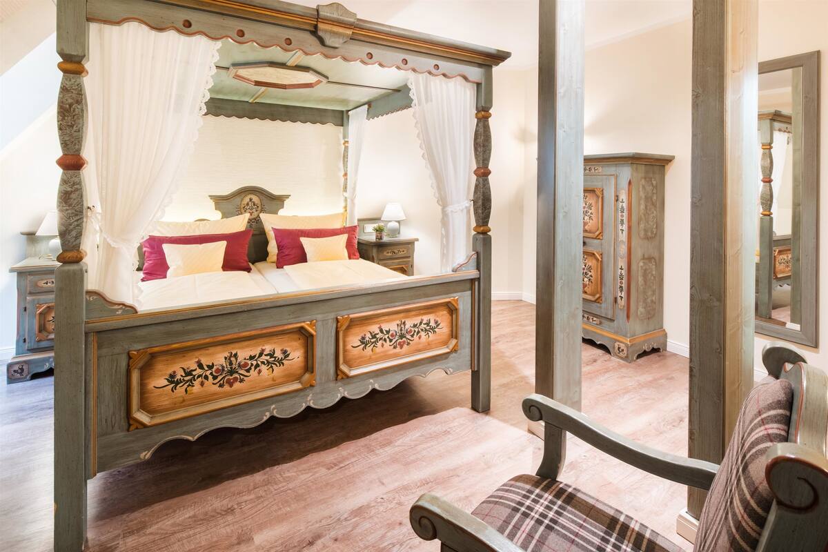 Un lit à baldaquin, une table de chevet en bois, une chaise et un miroir.