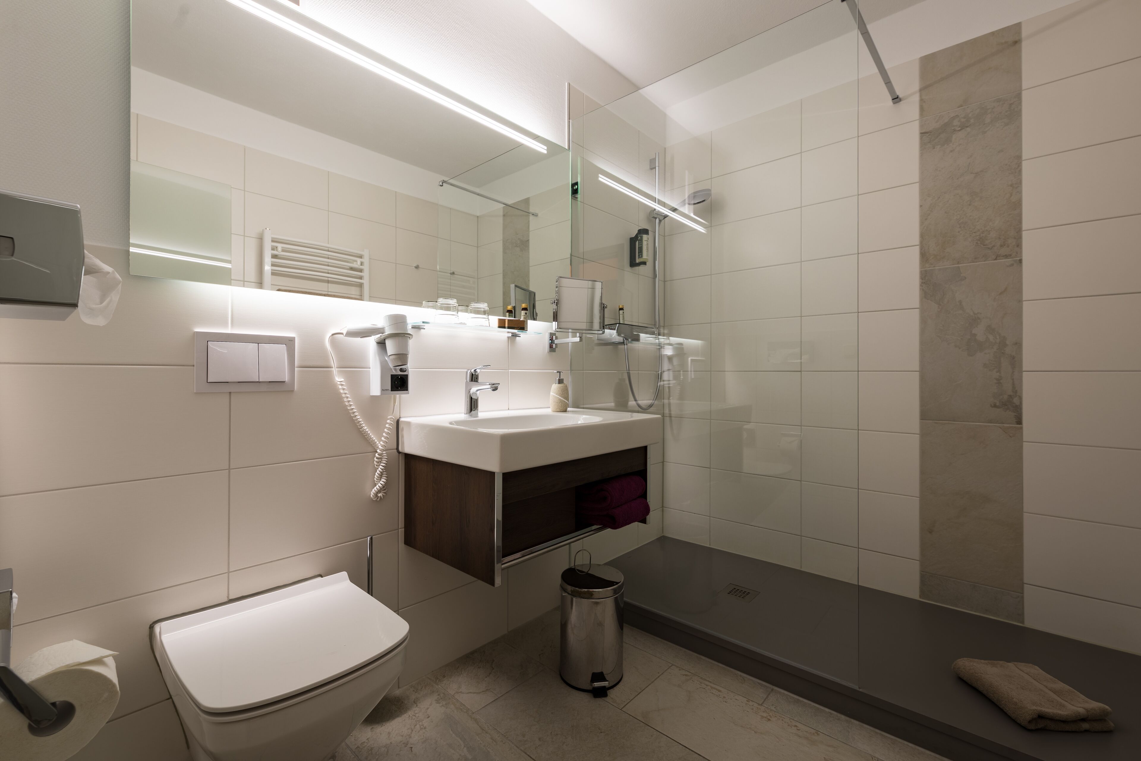 Une salle de bain moderne équipée de toilettes, d’un lavabo, d’un miroir et d’une douche.