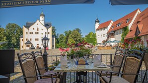 An outdoor dining area with wicker chairs and a table set for two, overlooking a historic building with a tower.