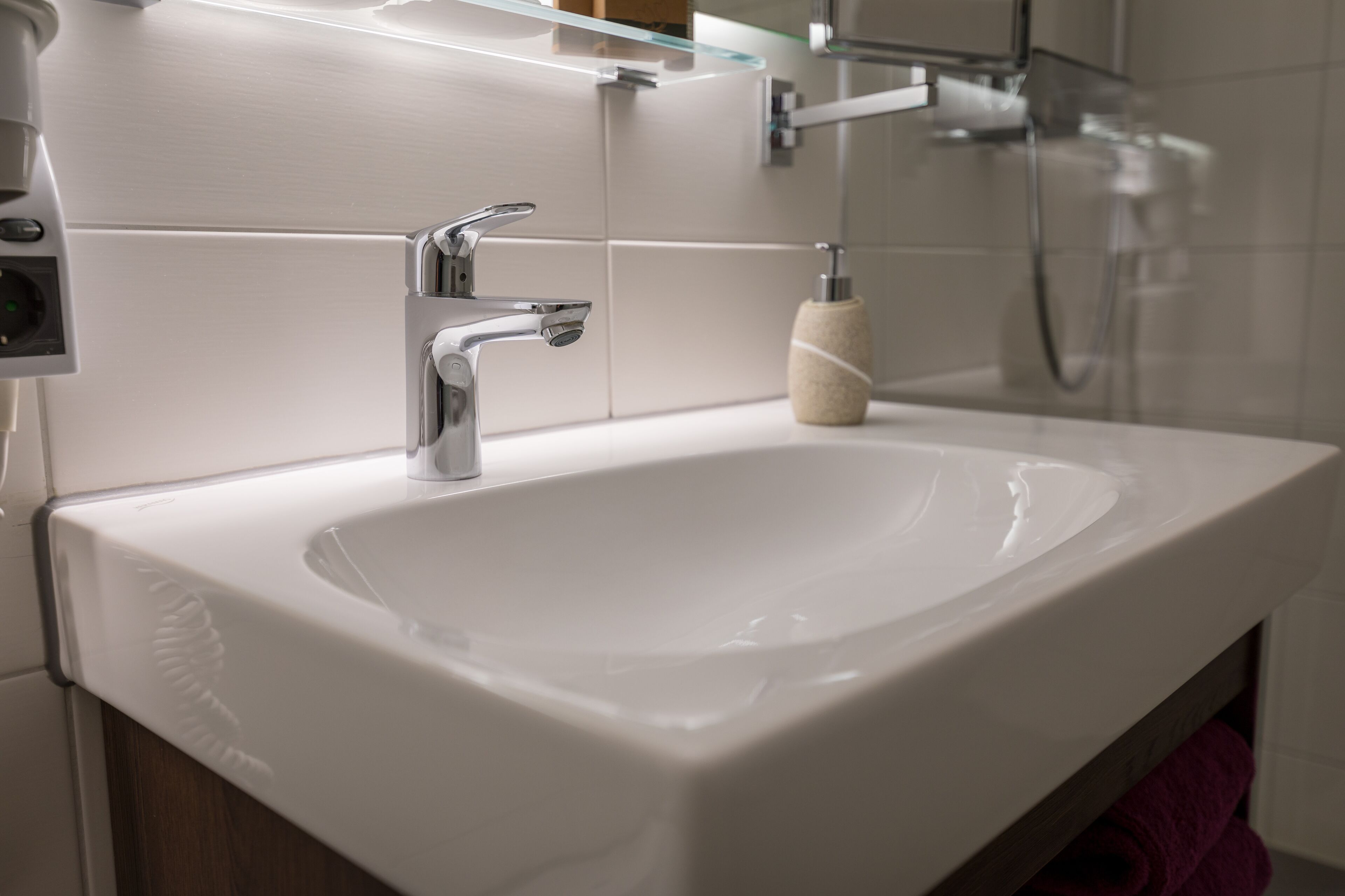 A modern bathroom with a white sink, chrome faucet, and a glass shelf above.