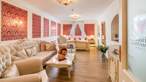 A luxurious room with a large sofa, a coffee table with flowers, a mirror, and a decorative wall. - Wasserschloss Klaffenbach Schlosshotel (Chemnitz)
