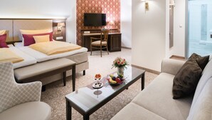 A hotel room with a bed, a sofa, a desk with a chair, a television, and a small table with a vase of flowers.