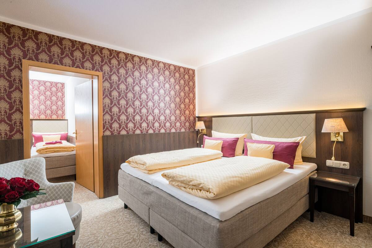 Une chambre d’hôtel avec un grand lit, une table de chevet avec une lampe, une chaise et un bureau agrémenté d’un vase de fleurs.