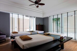 A hotel room with two beds, a ceiling fan, and large windows with blinds.