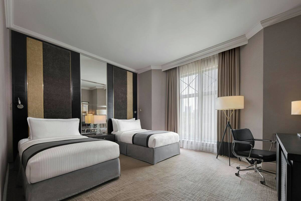 A hotel room with two beds, a desk, and a chair.