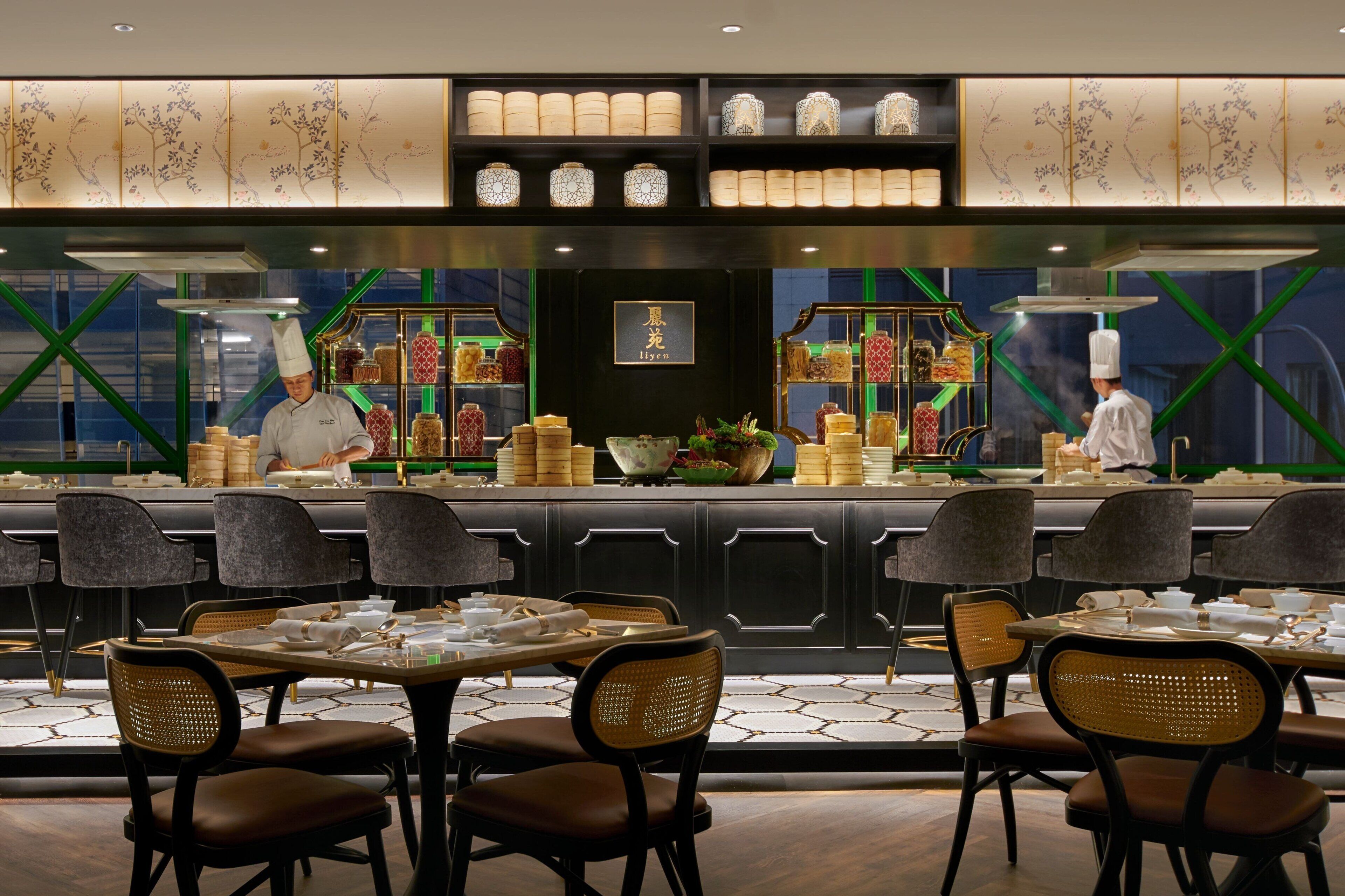 A restaurant with a modern interior, featuring a counter with chefs preparing food, and tables set for dining.