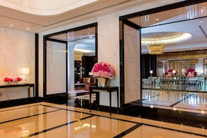 A spacious lobby with marble flooring, a reception desk, and a large floral arrangement.