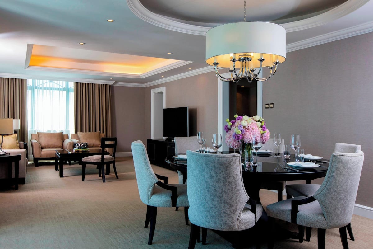 A hotel dining area with a round table, chairs, and a chandelier.