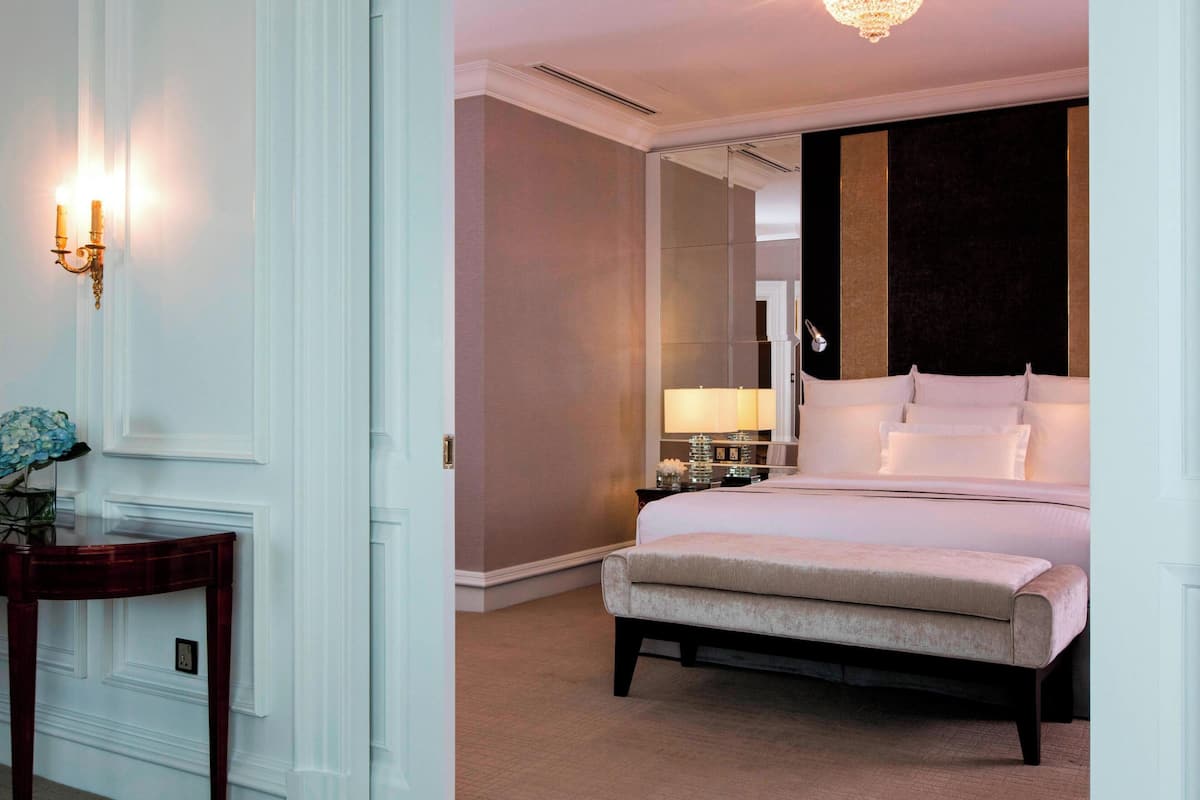 A hotel room with a large bed, bedside table, lamp, and a mirror.