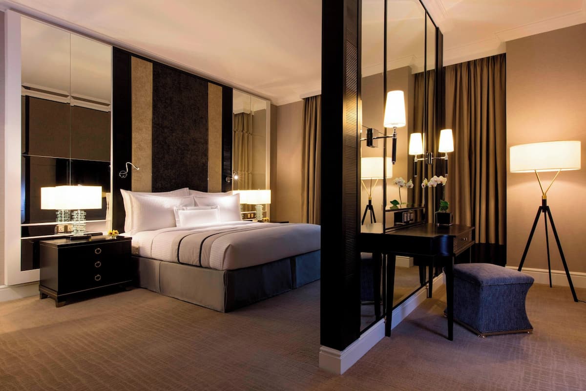 A modern hotel room with a large bed, bedside tables, a desk, a chair, and a mirror.