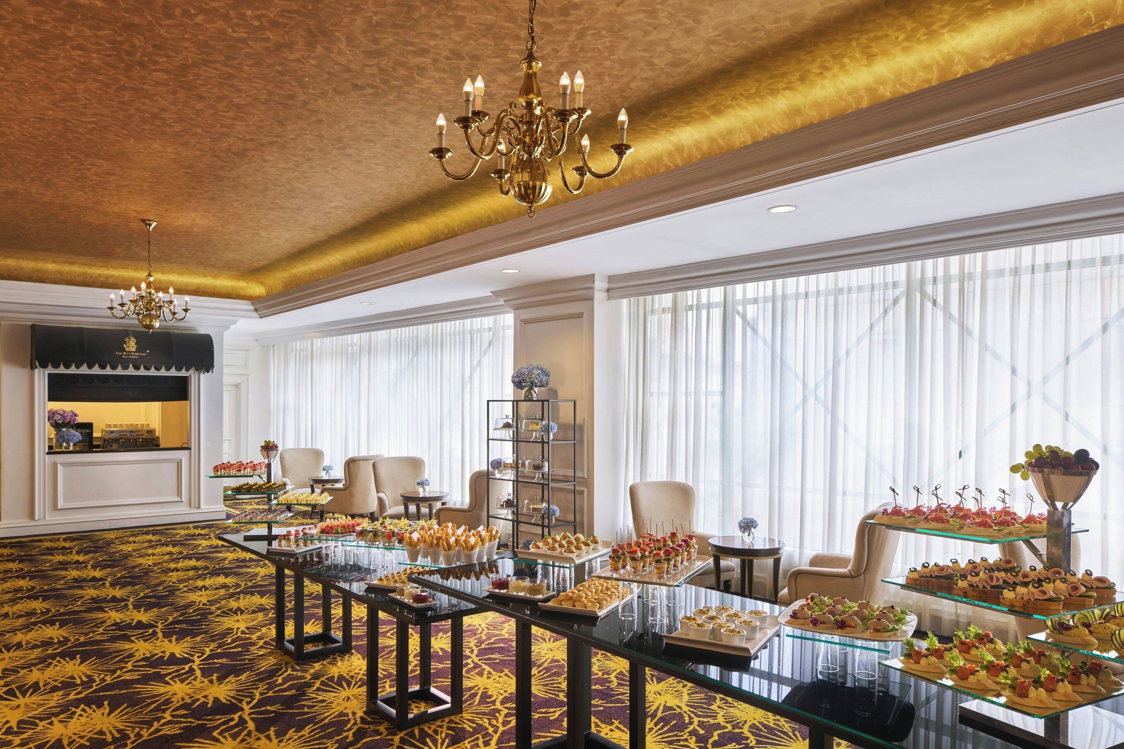 Een ruime kamer met een patroonbelegd tapijt, een kroonluchter en een buffet met diverse gerechten.