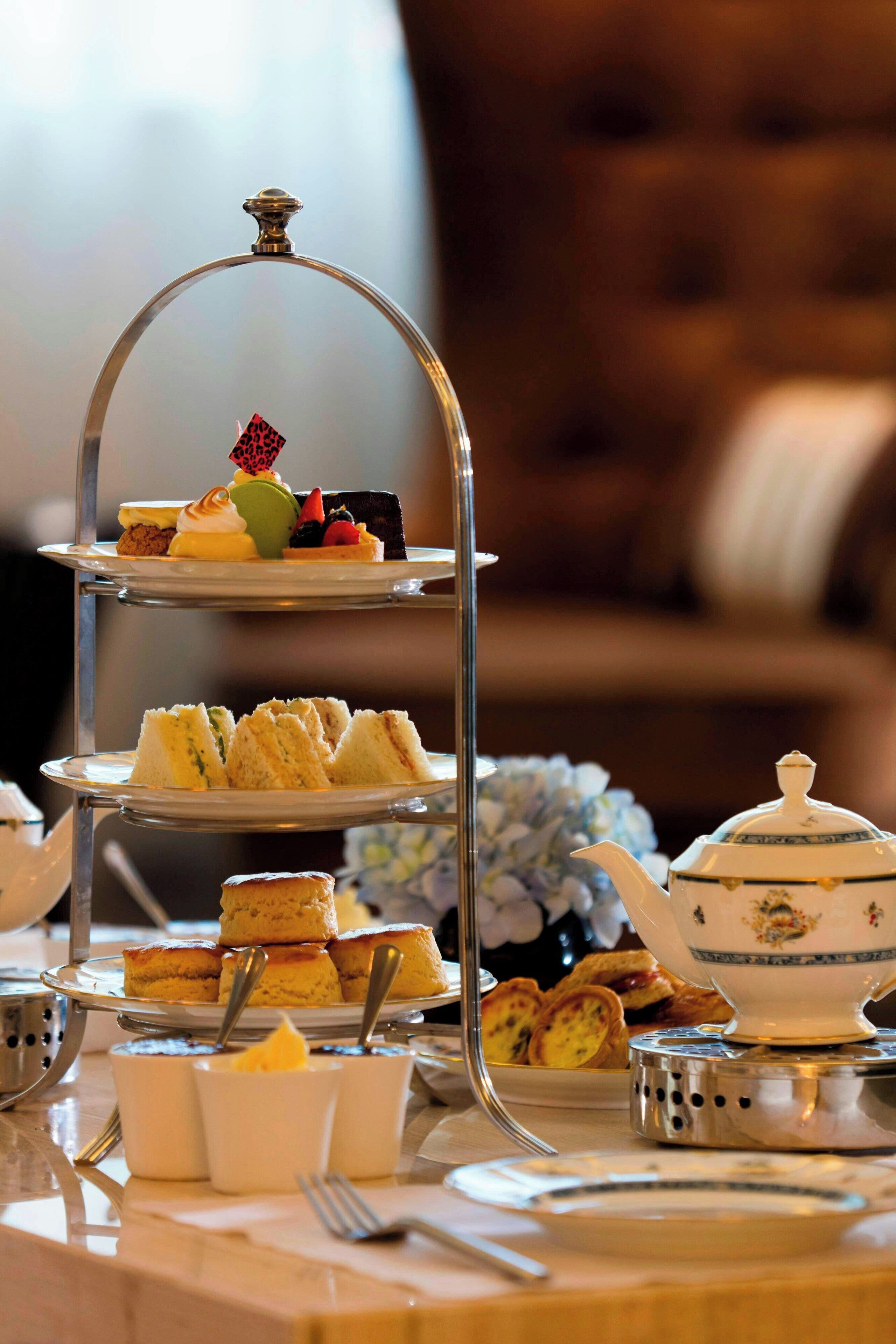 A three-tiered dessert stand with various pastries and a teapot on a table.