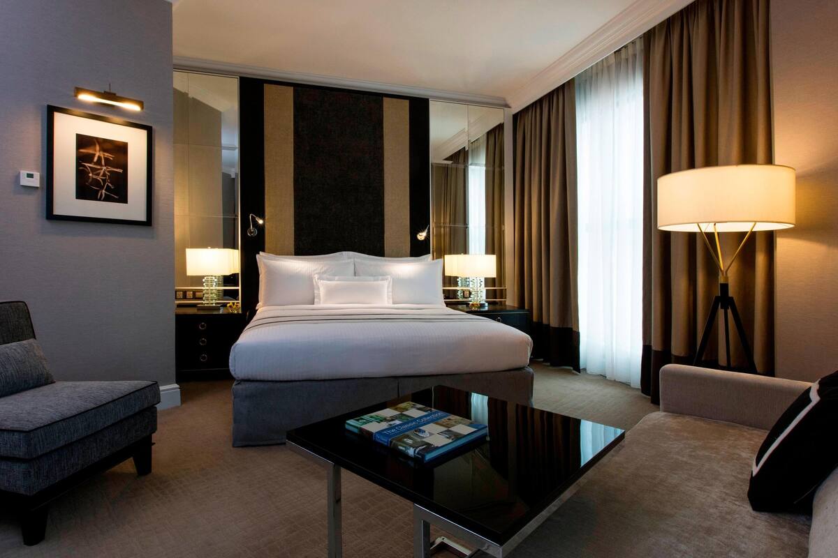 A hotel room with a large bed, a desk, a chair, a lamp, and a framed picture on the wall.