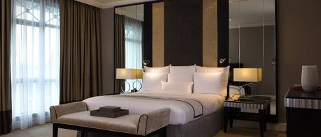 A modern hotel room with a large bed, bedside lamps, a nightstand, a bench, and a large mirror.
