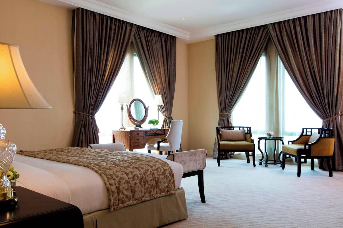 A hotel room with a large bed, two armchairs, a desk with a mirror, and a small table.