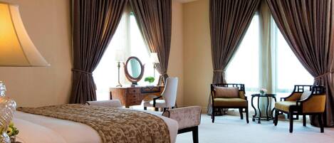 A hotel room with a large bed, two armchairs, a desk with a mirror, and a small table.
