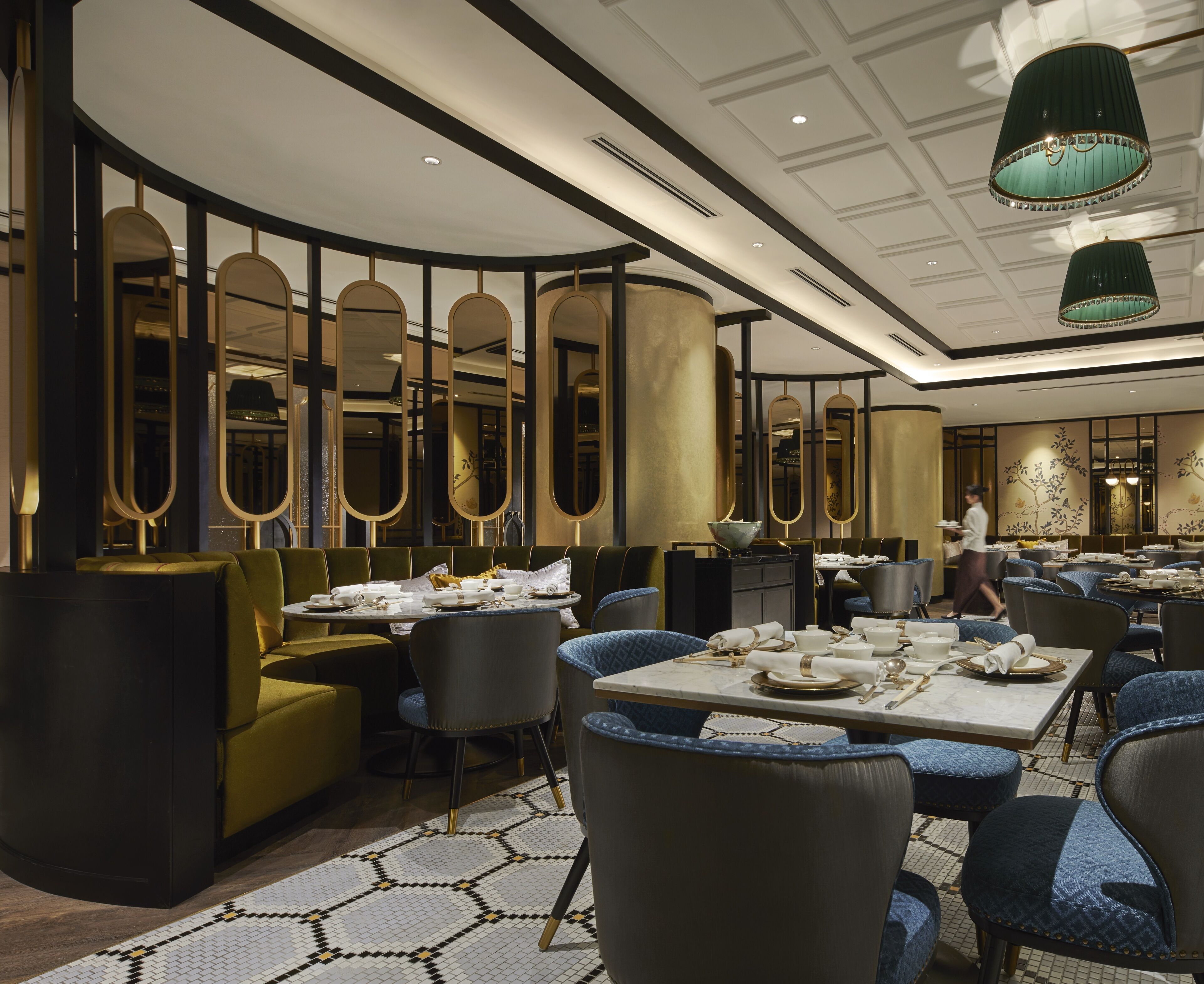 A modern dining area with round tables, blue upholstered chairs, and a woman serving food.