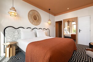 A modern hotel room with a large bed, two bedside tables, a round mirror, and a patterned floor.
