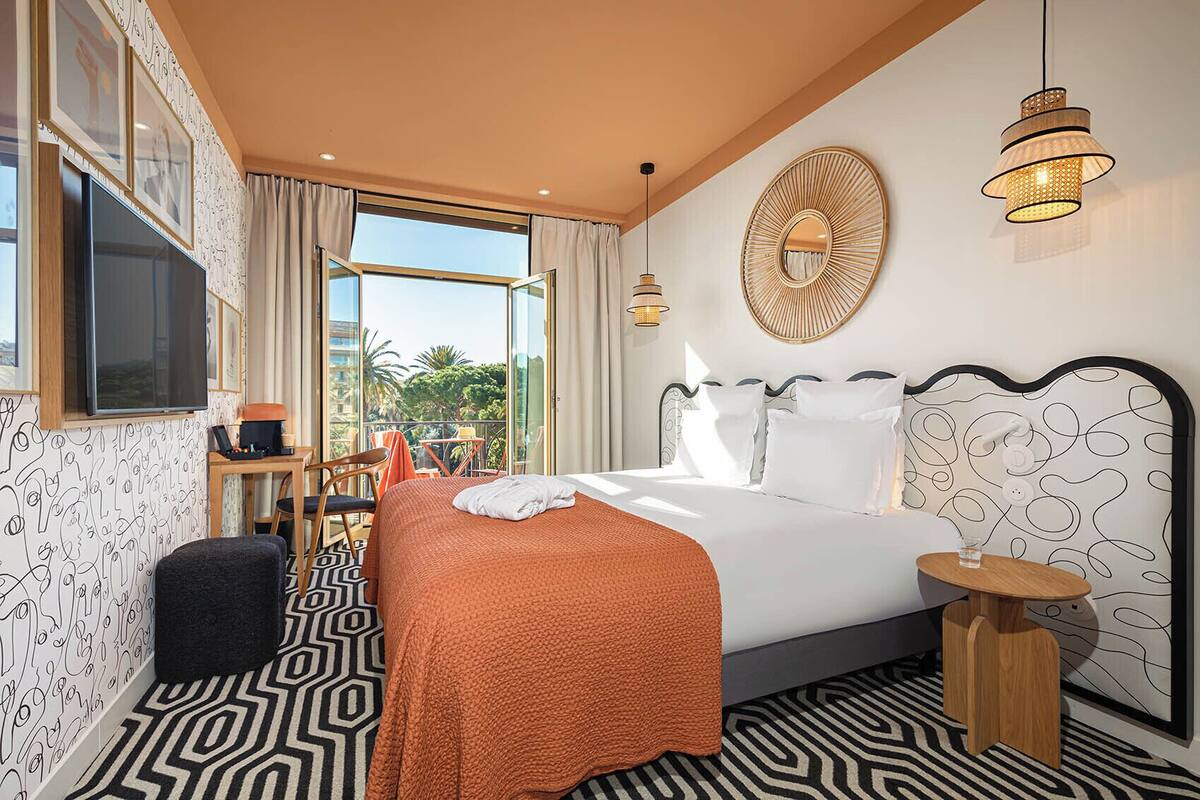Une chambre d’hôtel avec un grand lit, une télévision, un balcon avec une table et des chaises, et un sol à motifs.
