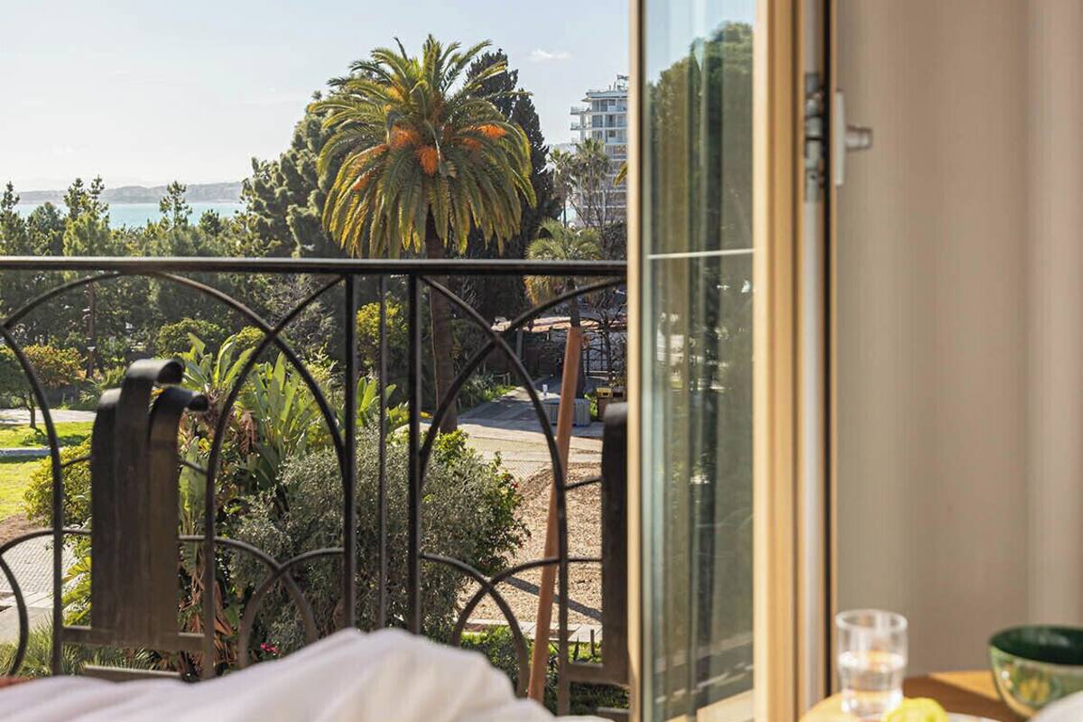 Un balcon donnant sur des palmiers et un bâtiment situé au loin.