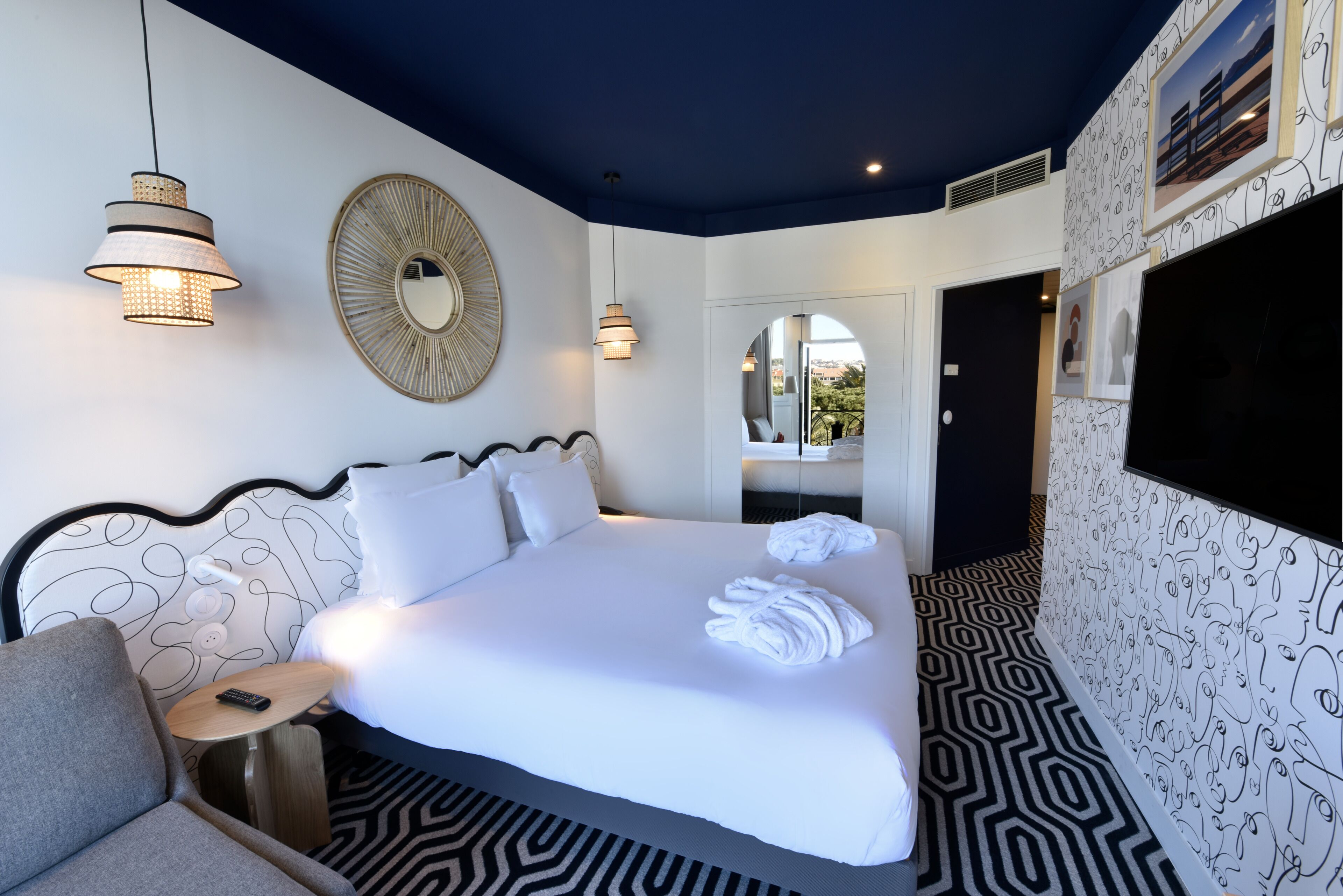 A modern hotel room with a large bed, a round mirror, and a patterned floor.