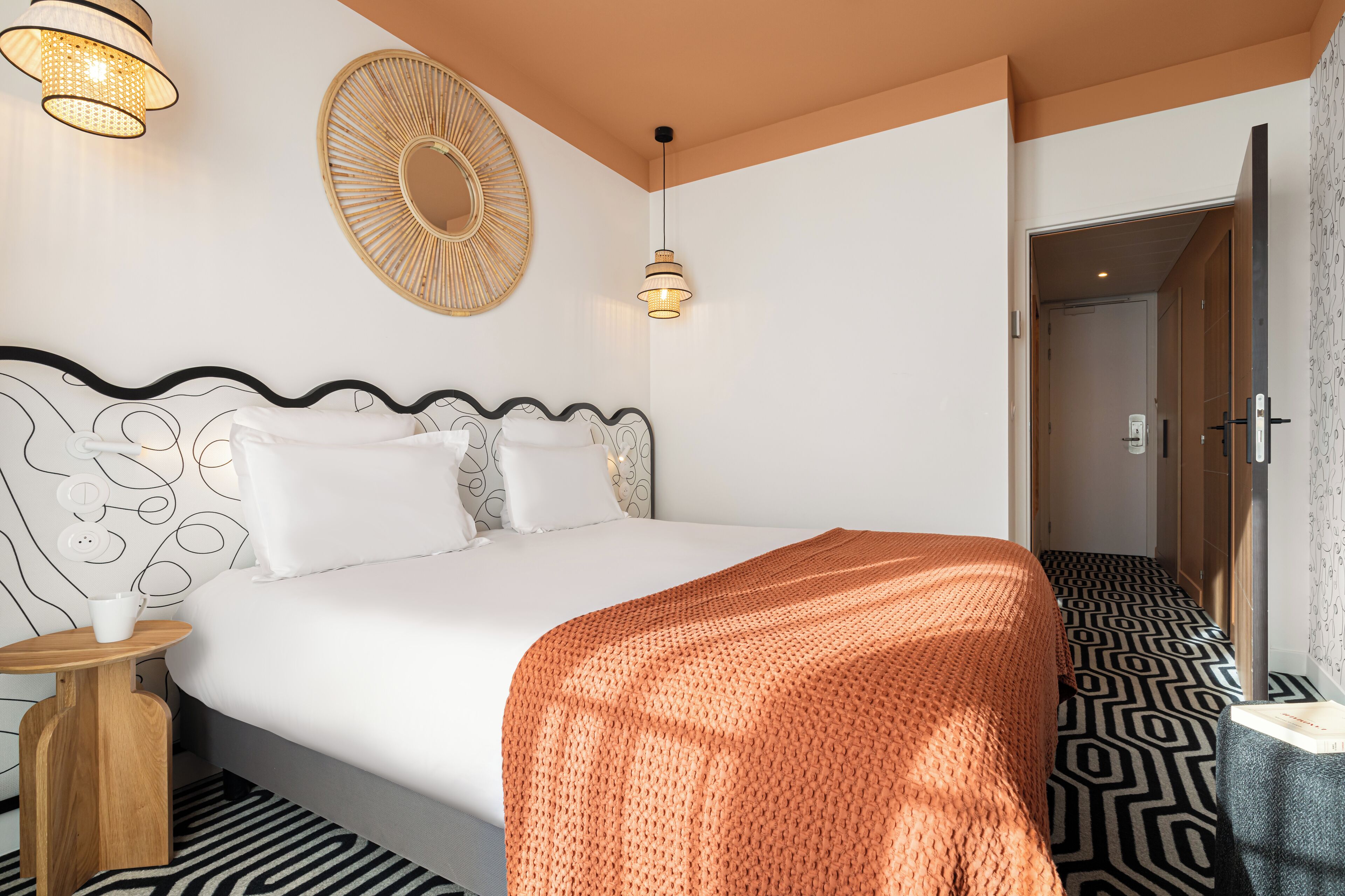 A modern hotel room with a large bed, a round mirror, and a patterned floor.
