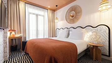 Habitación de hotel con una cama grande, una mesita de noche con lámpara, una pequeña mesa con una taza y un espejo en la pared.