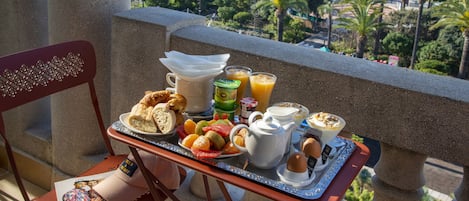 En balkon med et morgenmadssæt, der indeholder croissanter, frugt, juice og kaffe.