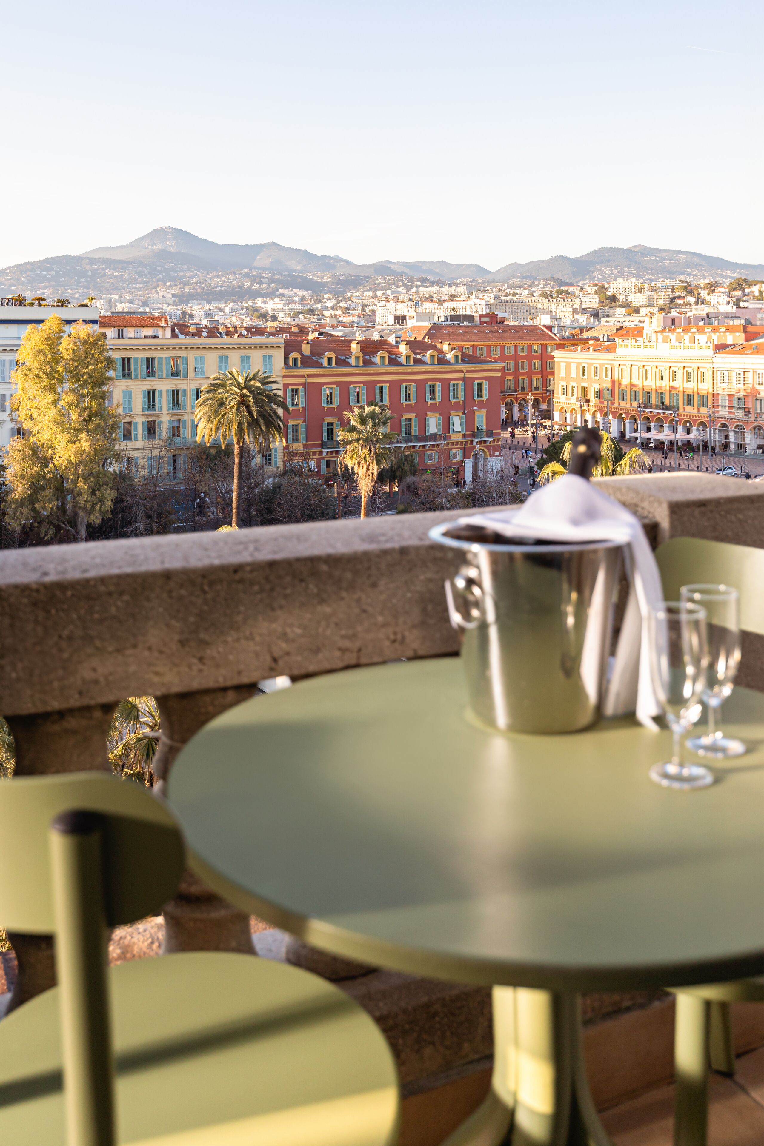 Una terraza con mesa y sillas, un cubo metálico y dos vasos.
