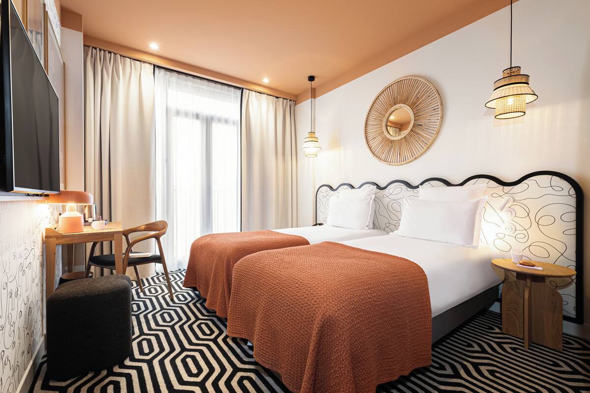 Une chambre d’hôtel comprenant un lit, deux tables de chevet, un bureau avec une chaise, une télévision et un sol à motifs.