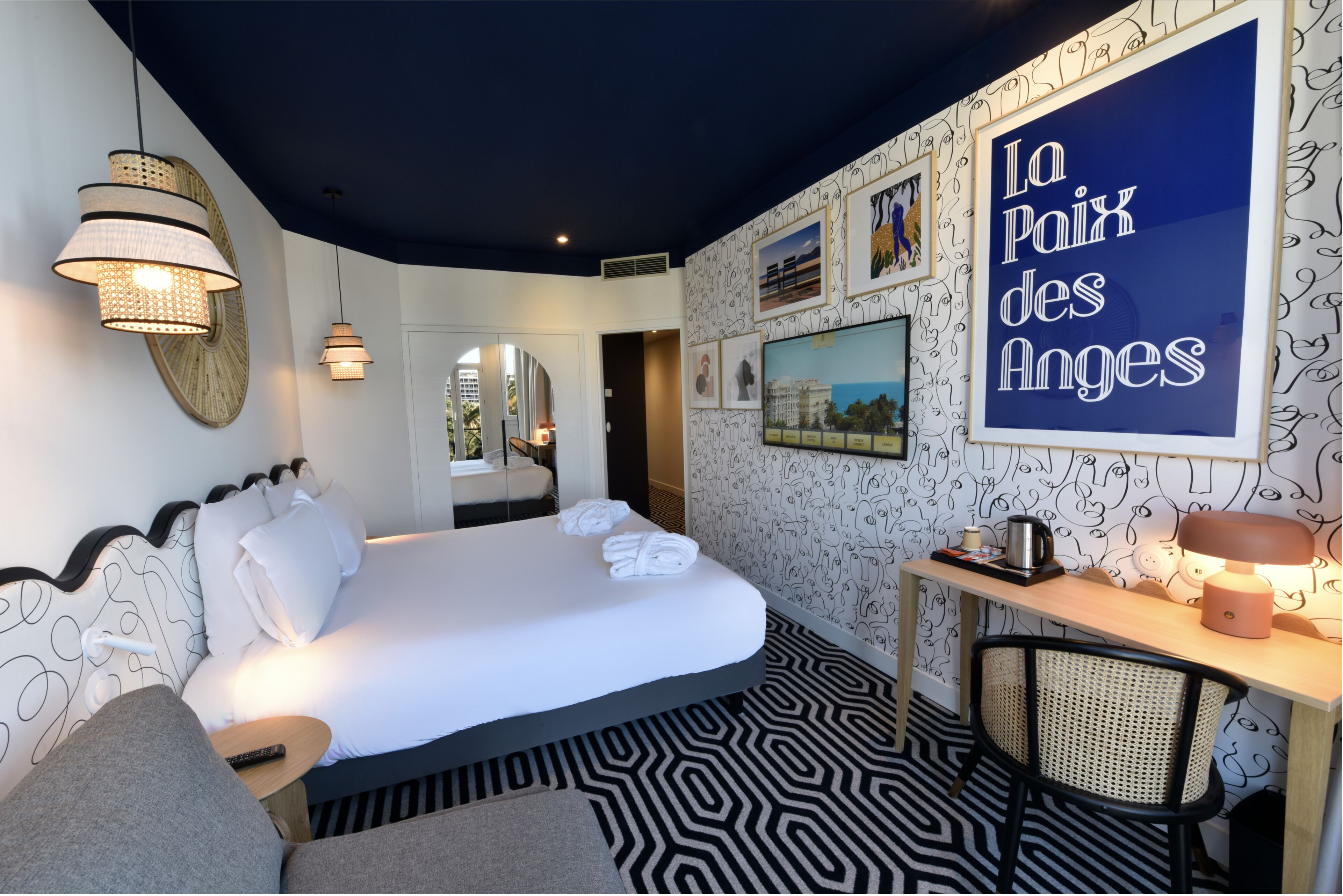 A hotel room with a bed, a desk, a chair, and a large framed sign on the wall.