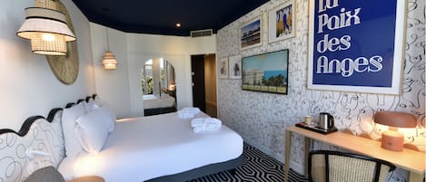 A hotel room with a bed, a desk, a chair, and a large framed sign on the wall.