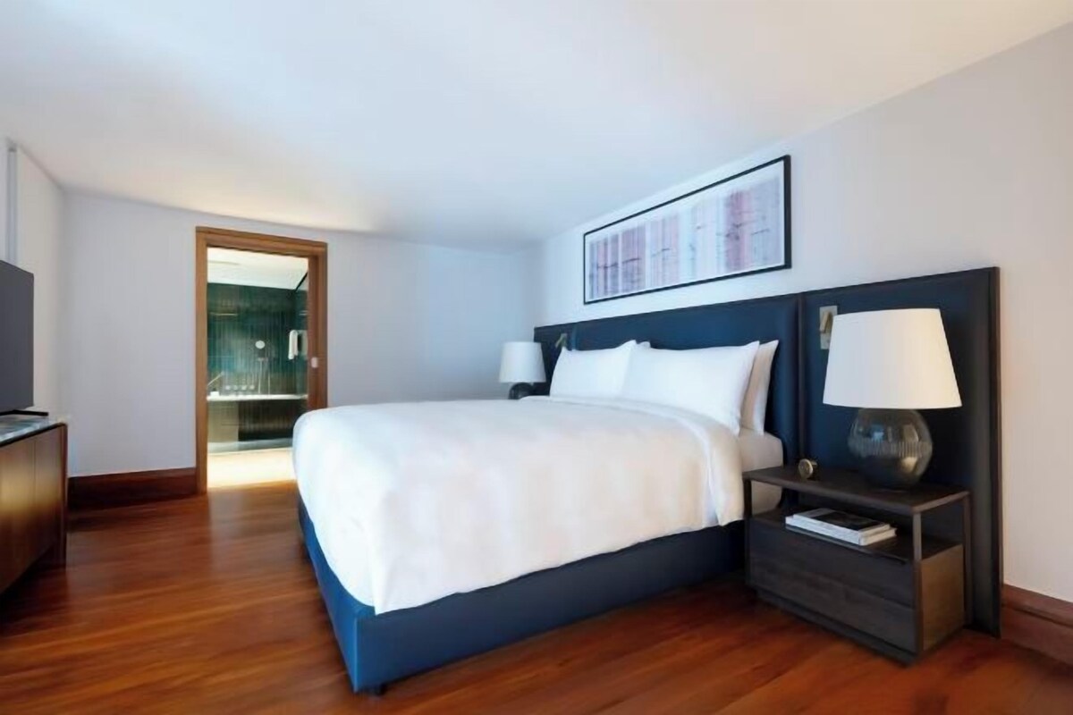 Camera d'albergo con un letto grande, comodini, televisione e una porta che dà su un balcone.