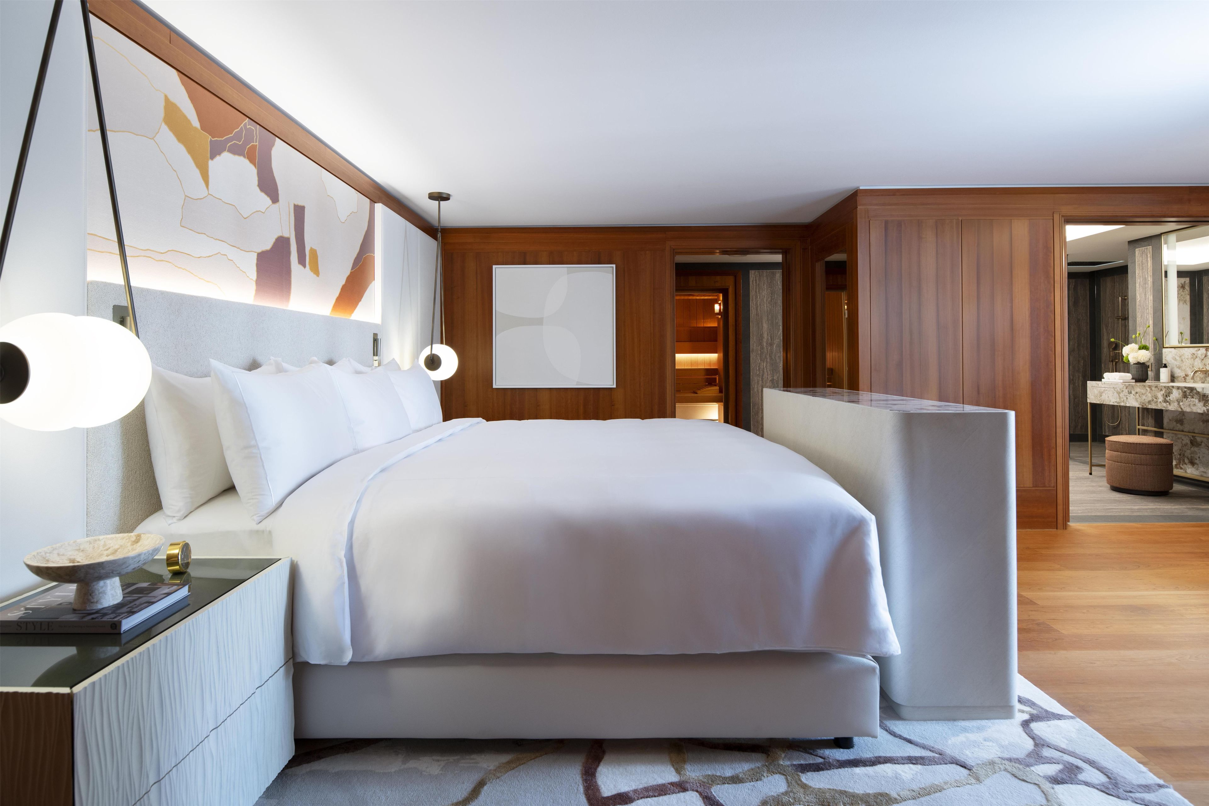A modern bedroom with a large bed, bedside lamps, a nightstand, and a view into a bathroom.